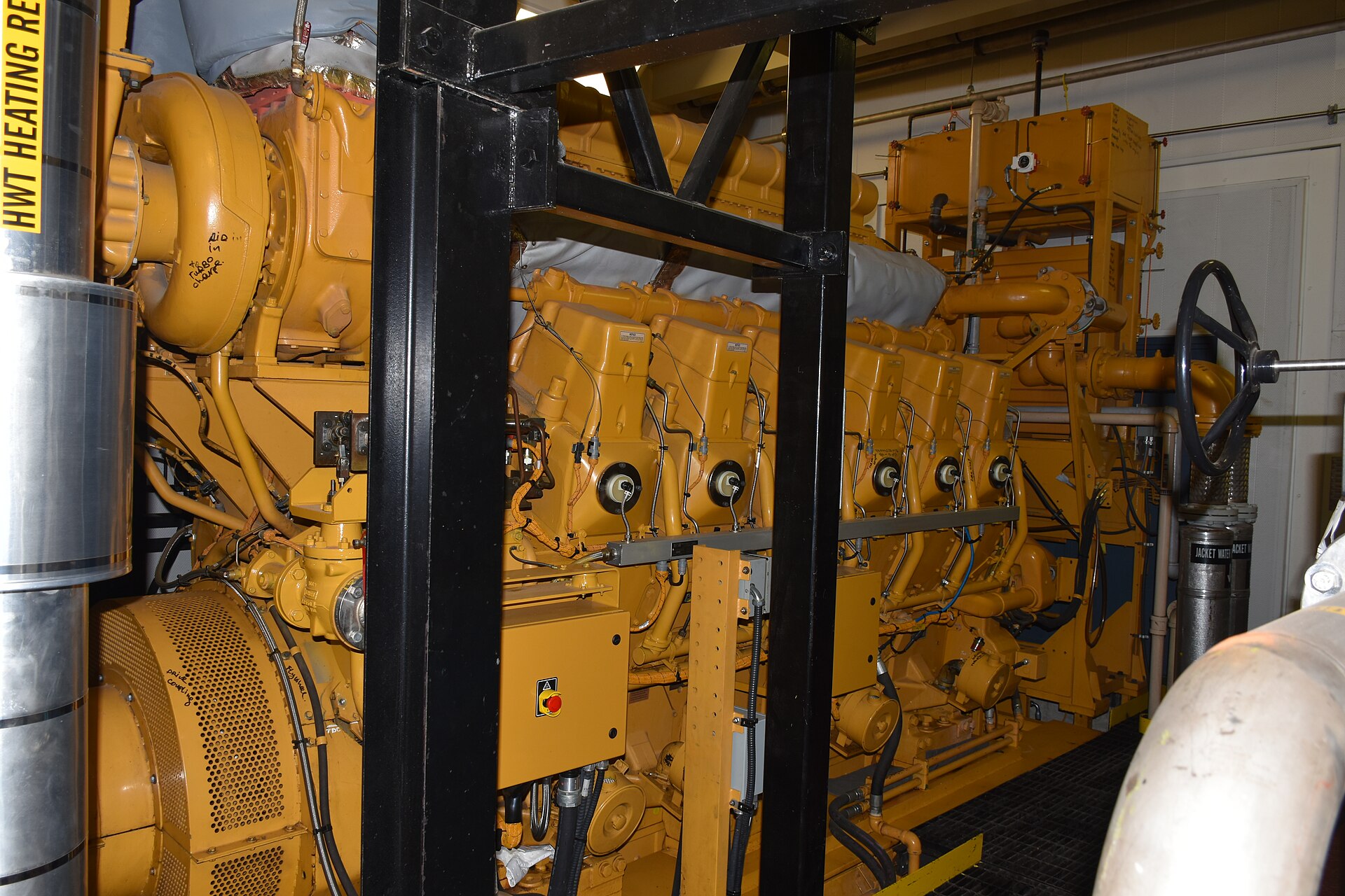 A yellow multi-cylinder generator engine in an equipment room